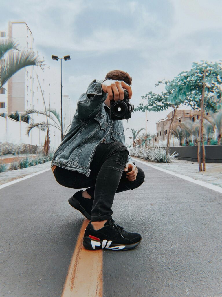 pexels-photo-1777479-1777479 A male model stylishly poses with a camera on a city street in an urban setting.