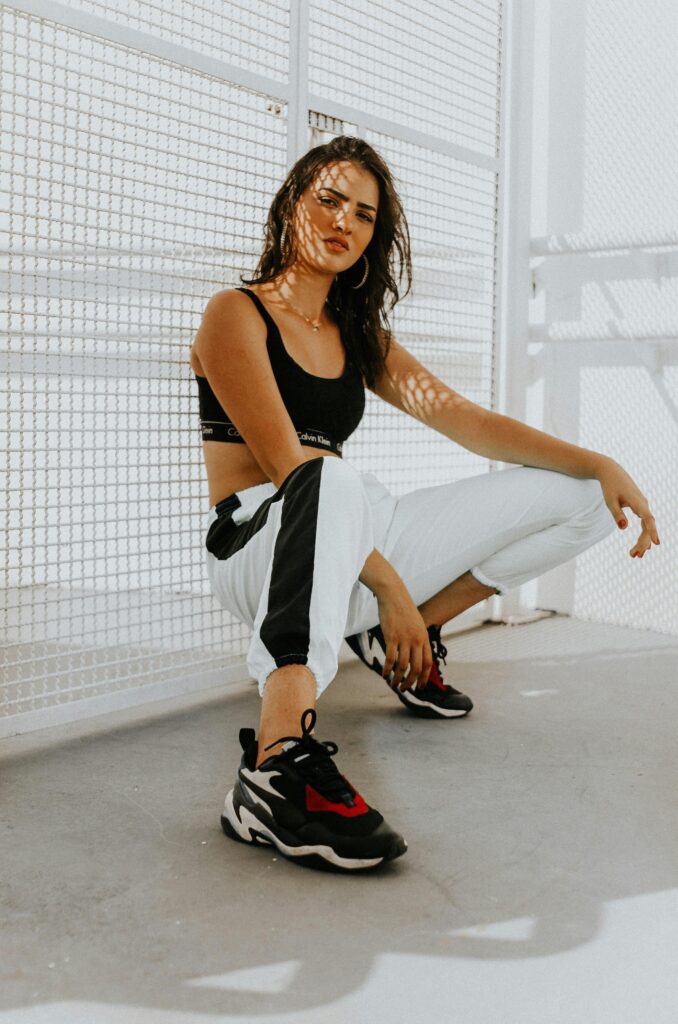 pexels-photo-1972115-1972115 Confident woman in urban attire, featuring trendy sneakers, crouching in sunlight.
