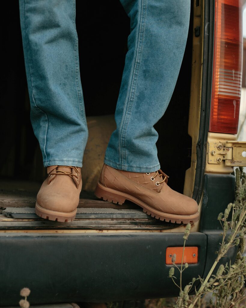 Man in jeans and boots standing in a van doorway, outdoors setting.