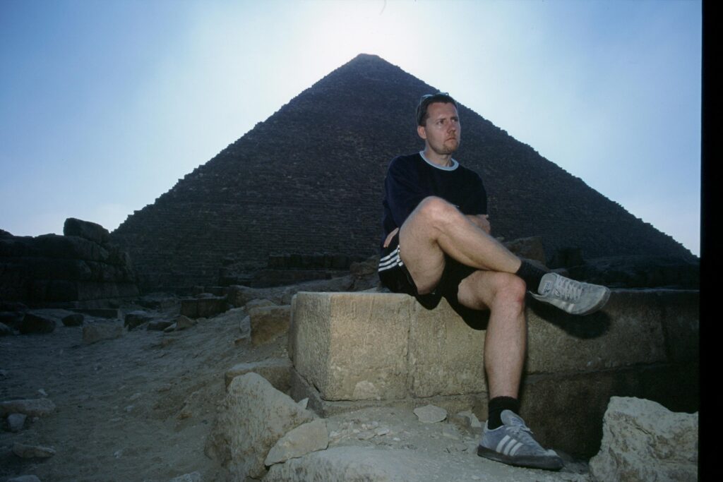 pexels-photo-2482321-2482321 Man sitting by a pyramid enjoying scenic desert landscape in Egypt.