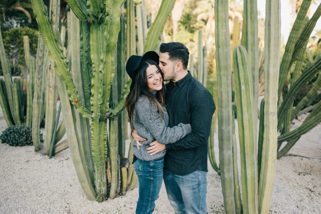 A joyful couple embracing among tall green cacti in an outdoor garden setting.